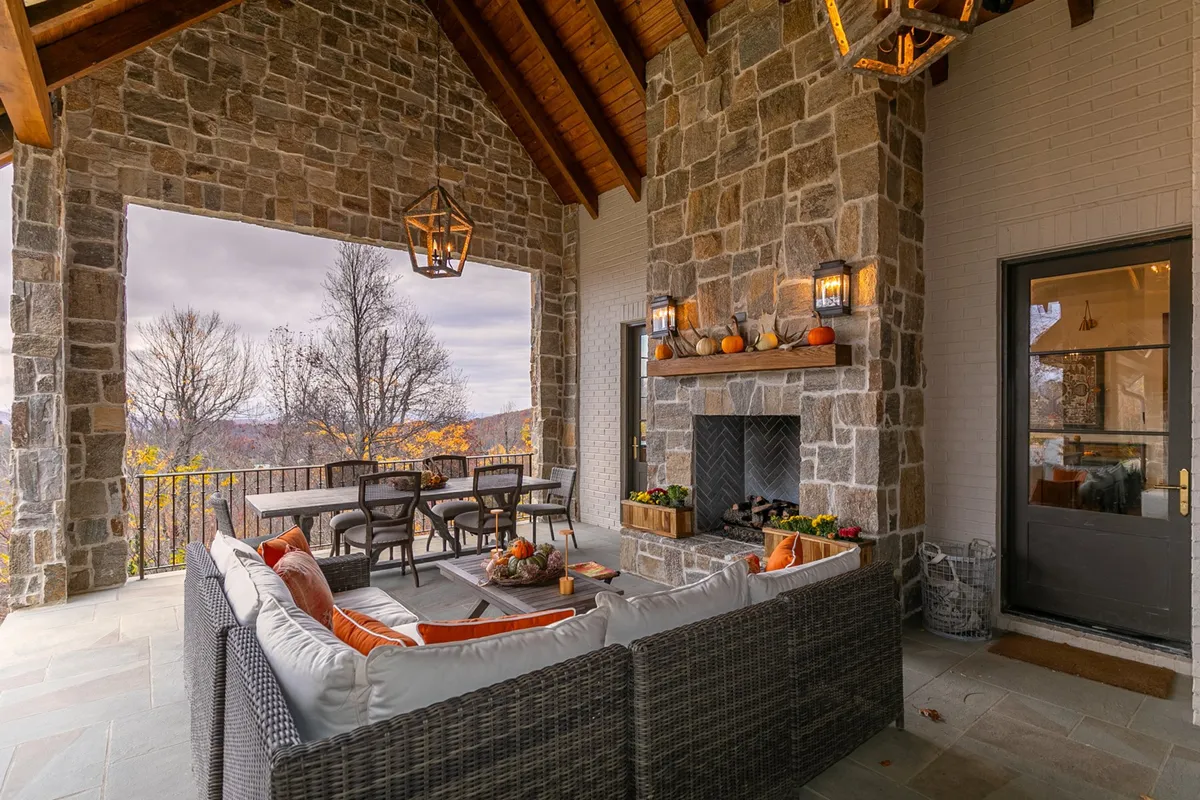 An outdoor patio area featuring a stone fireplace, ample seating, a dining table, and decorative lanterns. The setting is designed for gatherings and relaxation, with a scenic mountain backdrop that captures the spirit of mountain living and alfresco enjoyment.