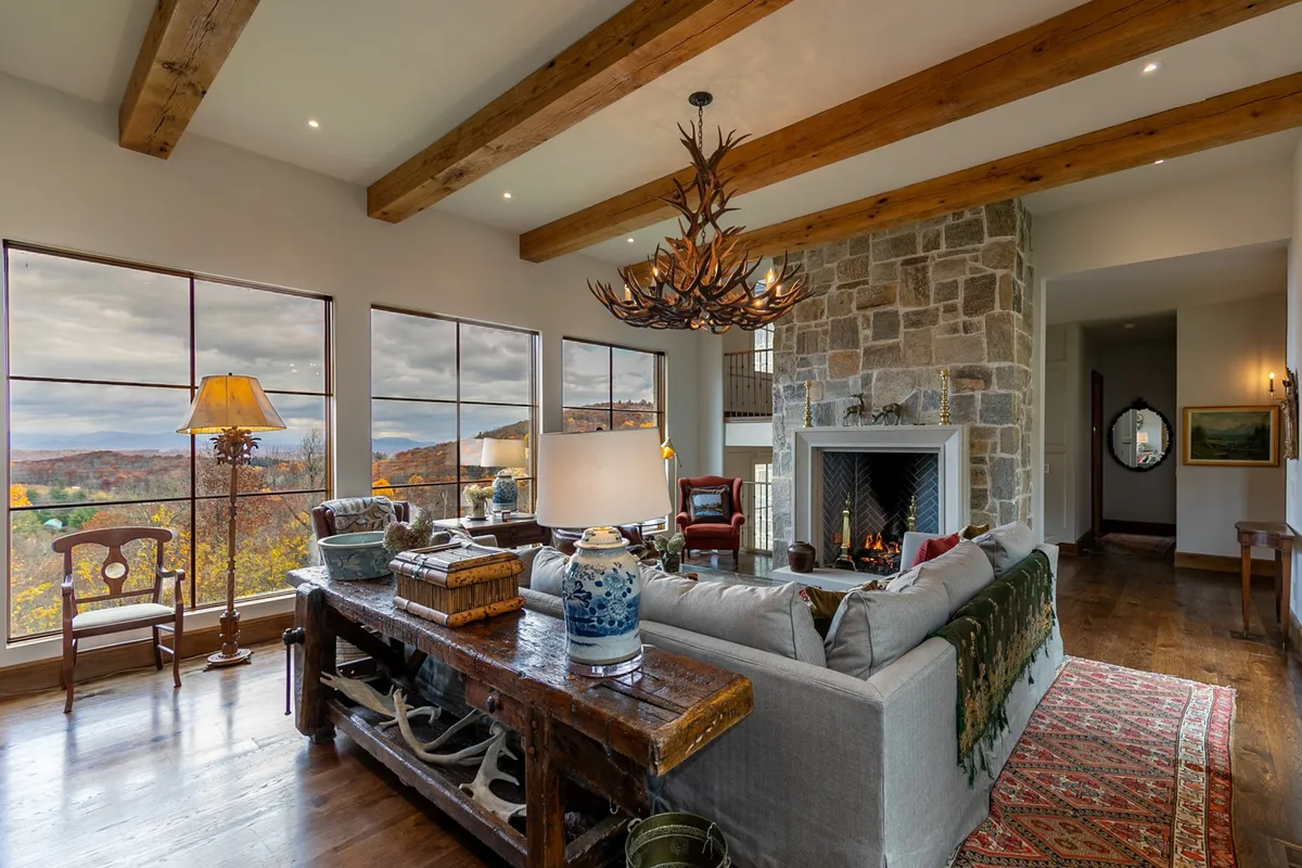 A warm and welcoming living space that centers on a prominent fireplace, with comfortable seating arranged to enjoy both the fire and scenic views from the windows. The chandelier adds a touch of elegance, and the overall styling encourages both relaxation and social interaction.