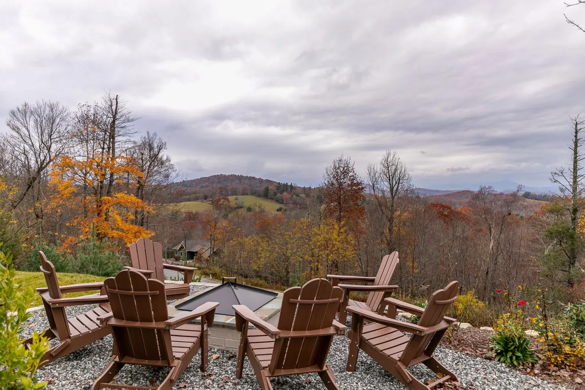 A cozy fire pit surrounded by Adirondack chairs, perfectly positioned to capture distant mountain vistas and autumn foliage. The scene invites gatherings for stargazing, storytelling, or enjoying warm drinks as the sun sets over the peaks.