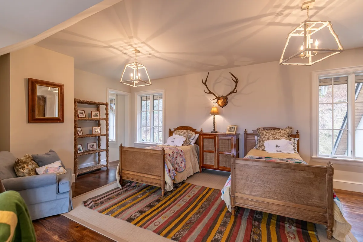 A warm, welcoming bedroom with two wooden beds adorned with cozy bedding and antler décor, a colorful rug, and a reading nook tucked by the window. The room exudes comfort and togetherness—perfect for families or groups.