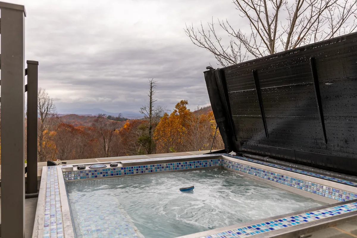 This exterior image captures a hot tub set on a deck overlooking sweeping mountain views, with vibrant fall foliage in the distance. The tranquil scene suggests relaxation after a day of adventure, and the natural beauty of the Blue Ridge Parkway is on full display.