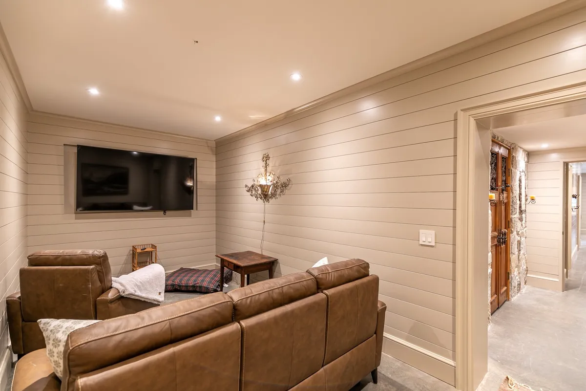 The image captures a media room with plush leather sofas, a large television as the focal point, a striking chandelier overhead, and a sturdy wooden table. The arrangement encourages socializing and relaxation, making it an ideal spot for movie nights or game sessions.