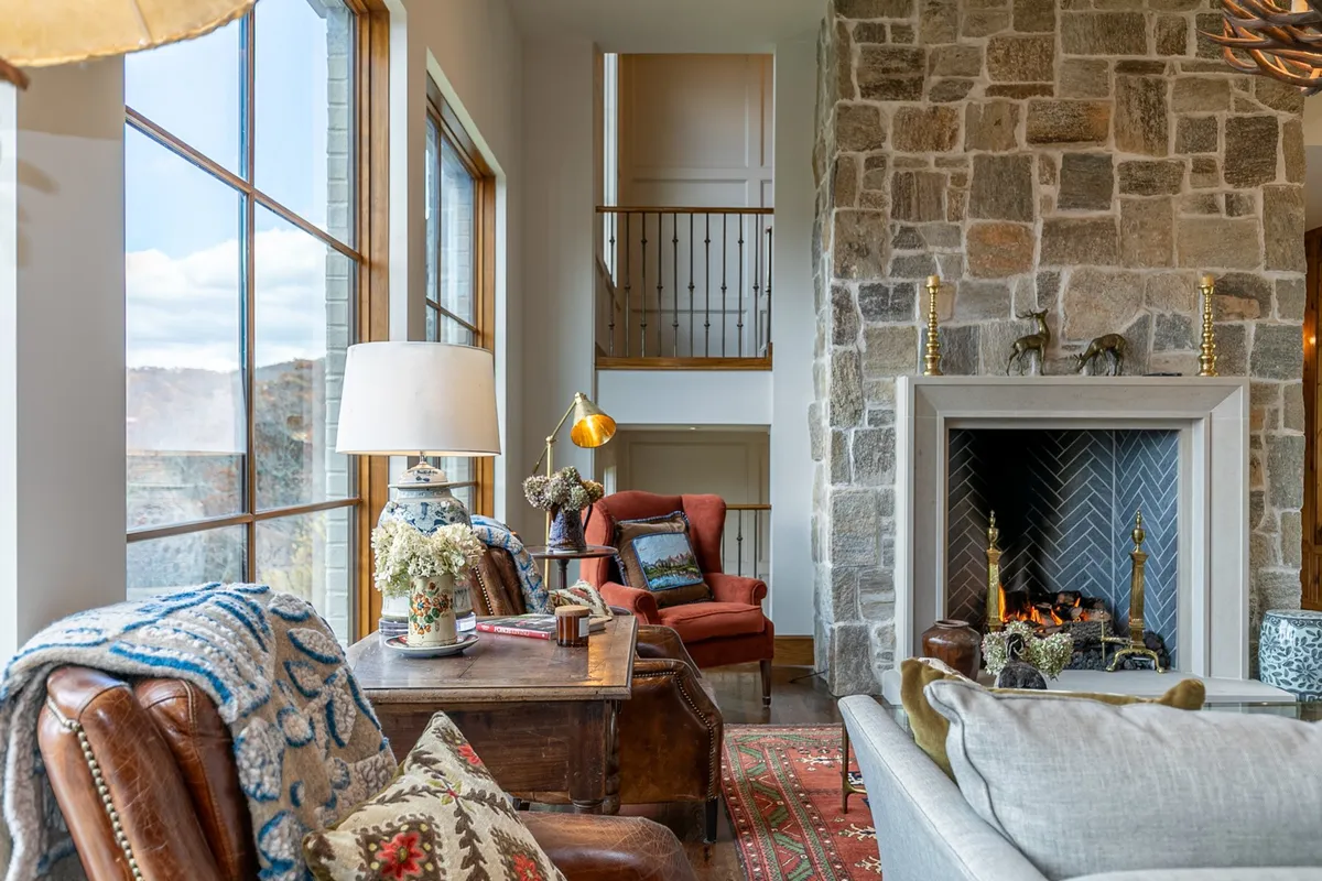 A spacious living area featuring a large stone fireplace, comfortable seating, and expansive windows that frame the surrounding landscape. The room is perfect for gatherings, whether for holiday celebrations or quiet mornings with coffee while watching the sunrise over the hills.