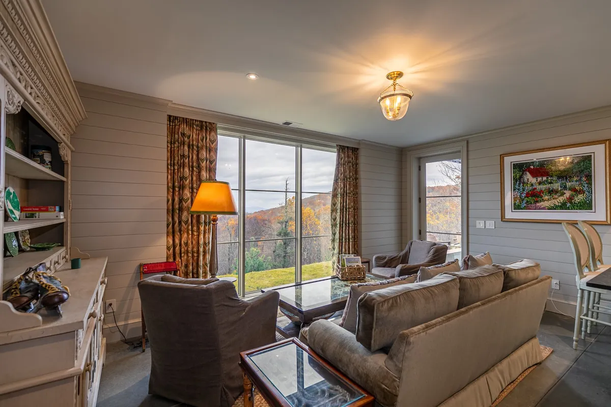 A comfortable seating arrangement faces large windows offering a scenic view, accented by decorative lamps and artwork. The inviting setup is ideal for casual conversations, enjoying the view, or relaxing after a group activity.