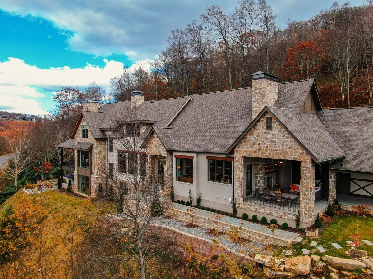 The photo highlights the lodge's stone facade, a cozy porch seating area, and the sweeping natural landscape around the property. The scene evokes both the welcoming entry point for guests heading out to explore and a relaxing space to enjoy the surrounding wilderness.